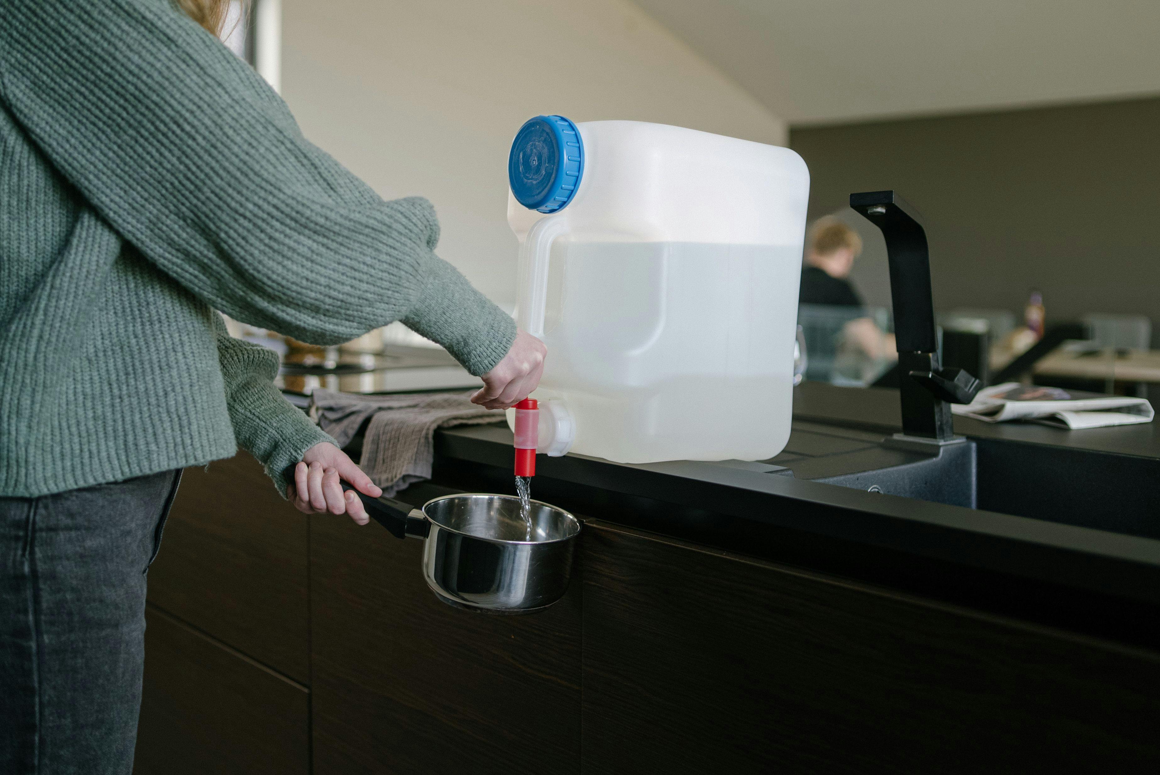 A large water jug stands on the kitchen counter next to a water tap where water has been running.