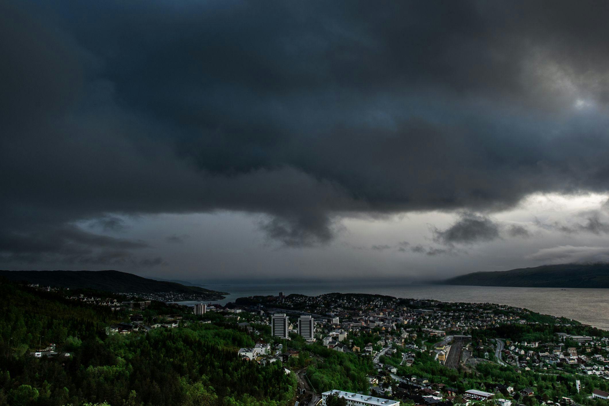 Fra en utsikt ser vi utover Narvik, det er grått og mørkt med tunge skyer over byen.